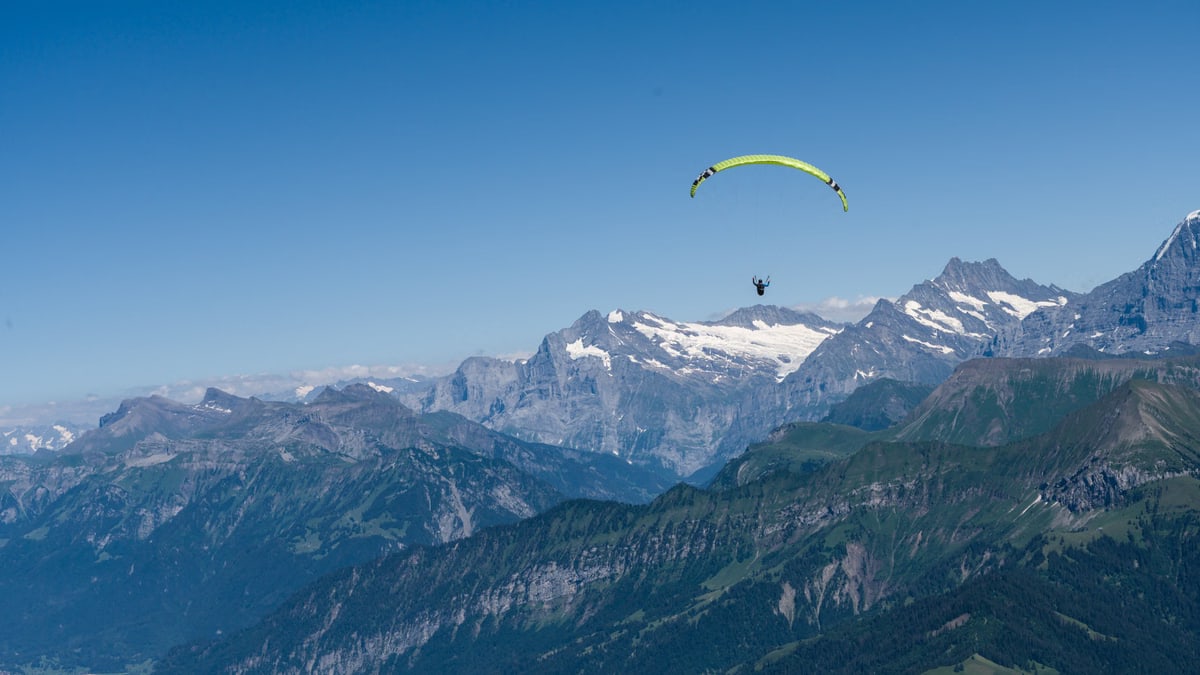 A paraglider soaring above the picturesque Swiss Alps with clear blue skies and stunning mountain views.